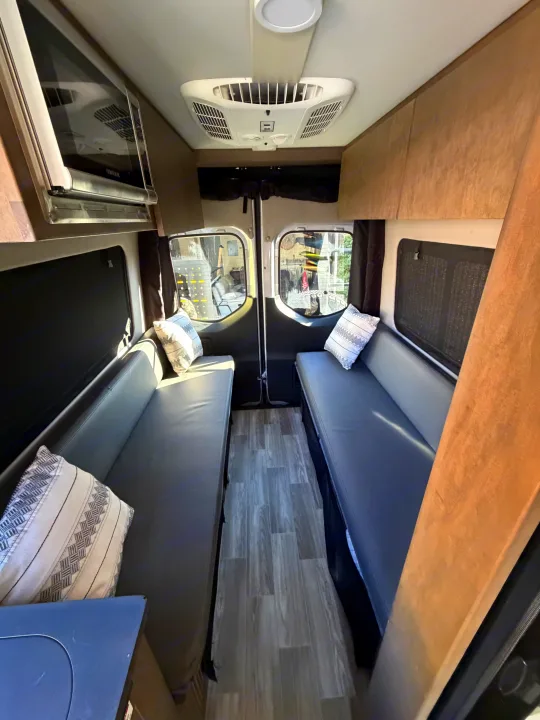RV rental interior with facing benches, convertible bed, overhead microwave, and AC unit. Features wood-look flooring.. Cahaba Cahaba Class B 2022