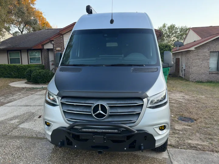 Frontal view of a silver Mercedes Sprinter van, black hood, custom bumper, light bar, yellow fog lights. Ideal rv rental.. Cahaba Cahaba Class B 2022