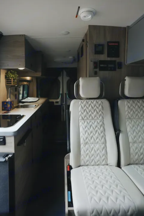 Explore this modern rv rental interior, featuring bright quilted seats, a compact kitchen, and overhead control panel.. Winnebago Winnebago 2026