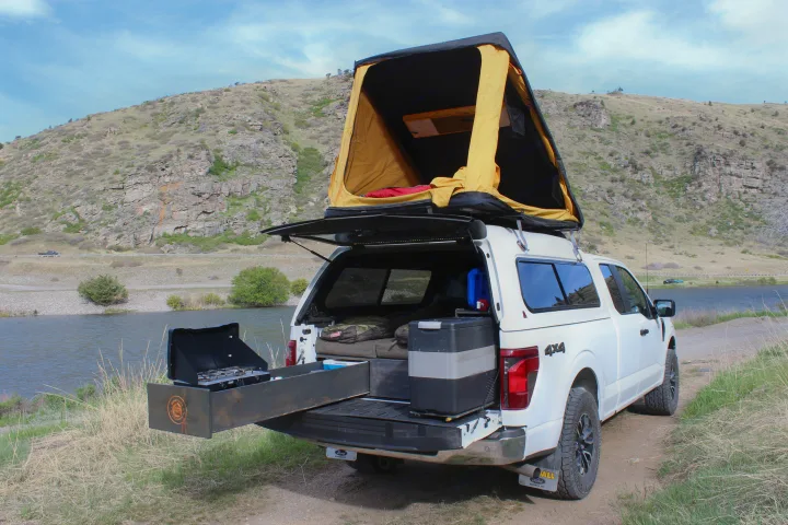 Overlanding truck with rooftop tent & outdoor kitchen by a scenic lake, perfect for an RV rental adventure.. Ford Ford F150 2024
