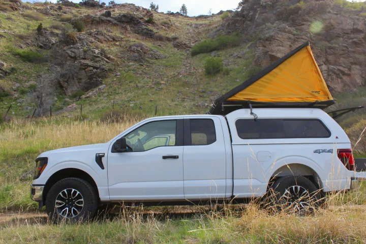 White F-150 truck, with a yellow rooftop tent & camper shell, ideal for your next rv rental adventure in nature.. Ford Ford F150 2024