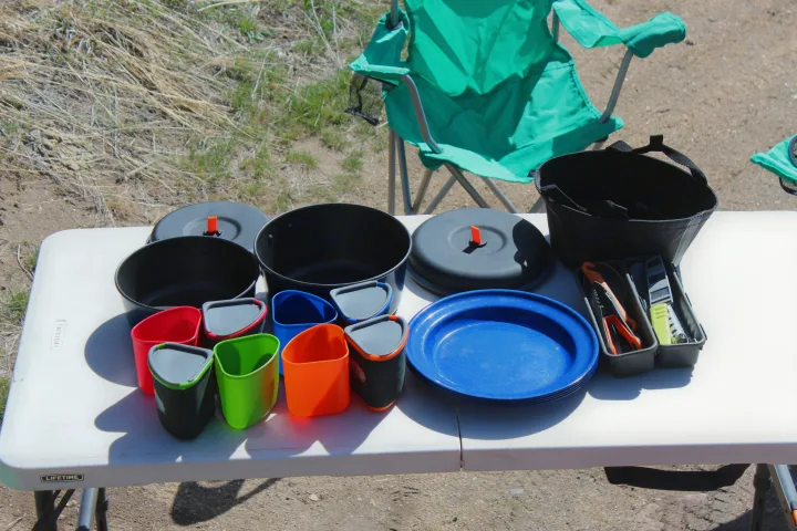 Essential camping kitchen gear for your RV rental: pots, colorful mugs, plates, and utensils on a white table.. Ford Ford F150 2024