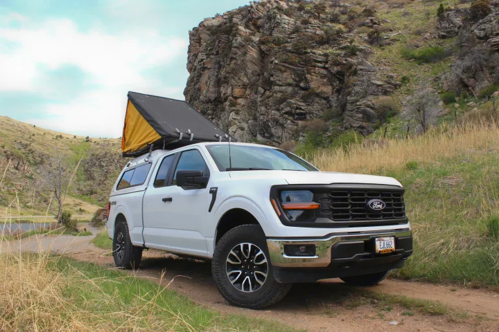 A white Ford F-150 truck with a rooftop tent on its camper. Ideal for an RV rental or off-road adventure through rocky terrain.. Ford Ford F150 2024