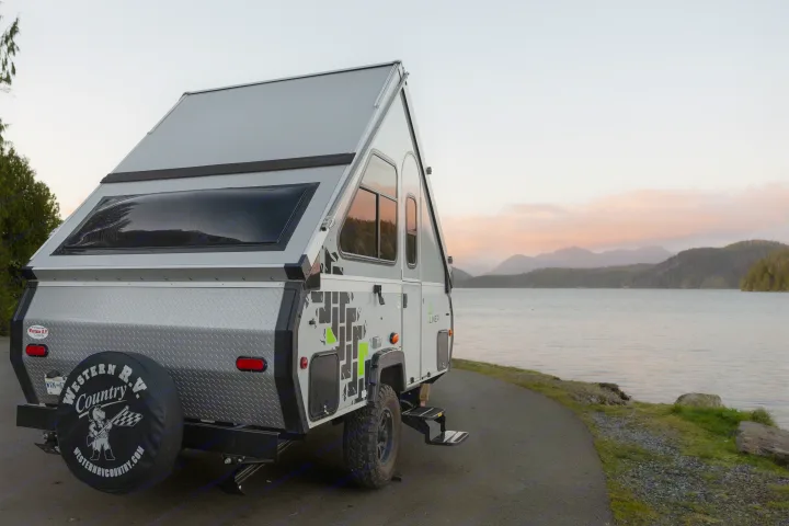 An A-frame RV rental, with an off-road design, parked lakeside at sunset. Ideal for scenic camping and travel adventures.. A Liner Scout 2026