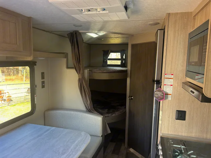 RV rental interior: Bright dinette, bunk beds with privacy curtain, and compact kitchen appliances. Ready for comfortable travel.. Coachmen Catalina 2025