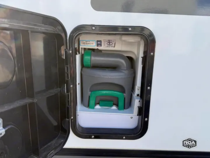 Easy waste disposal for your RV rental: An open hatch reveals a grey and green portable toilet cassette in an RV.. nuCamp T@B 2022