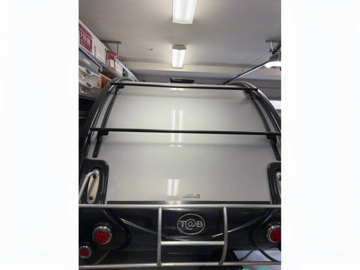 Rear view of a T@B travel trailer in a garage, featuring a roof rack and ladder. This type of vehicle is popular for rv rental.. nuCamp T@B 2022