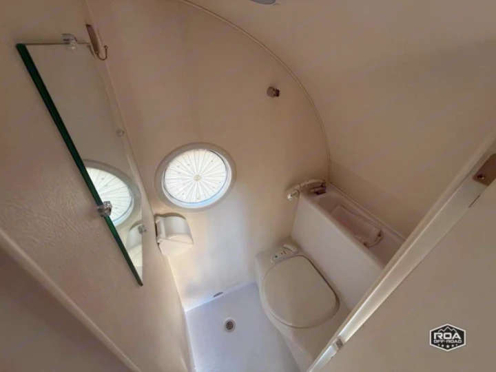 RV rental bathroom: compact toilet, shower, mirror, and ceiling vent in a small, white, self-contained space.. nuCamp T@B 2022