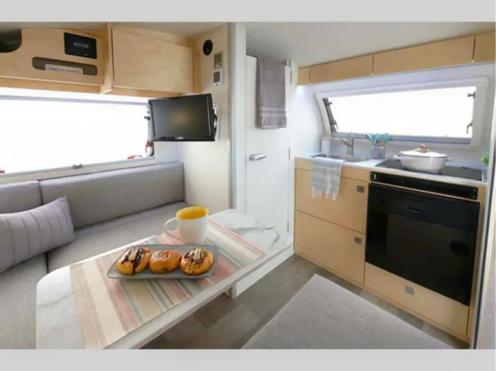 This modern RV rental interior features a compact kitchen, cozy dining/living area, and TV, perfect for travel.. nuCamp T@B 2022