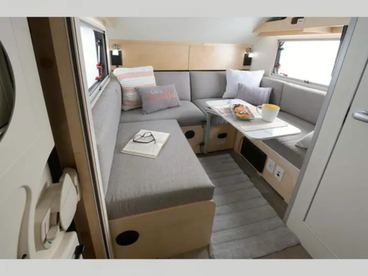 Cozy rv rental interior: a U-shaped dinette with gray cushions, table, book, and rug. Ideal for compact travel.. nuCamp T@B 2022
