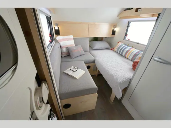 This RV rental's cozy interior features a gray sofa, bed, and light wood finishes, ideal for a comfortable camper trip.. nuCamp T@B 2022