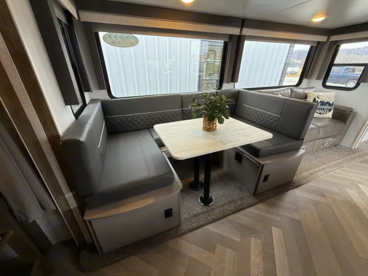 Modern RV rental dinette with gray U-shaped seating, light table, and large windows. Carpet & wood-look floor.. Forest River Salem 2022