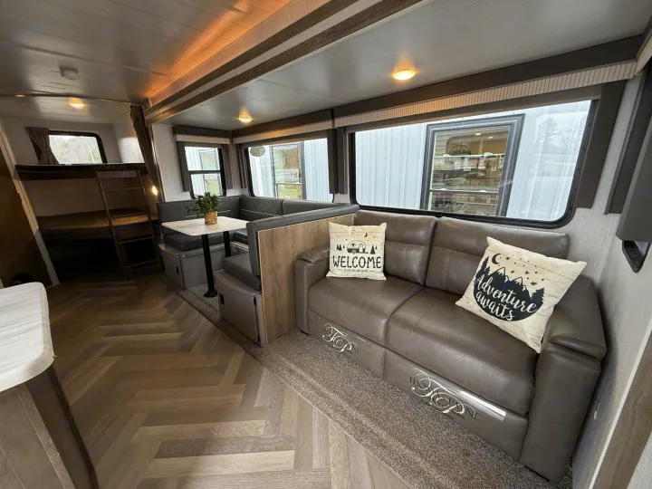 Spacious RV rental interior featuring a gray sofa, U-shaped dinette, bunk beds, and modern herringbone flooring.. Forest River Salem 2022