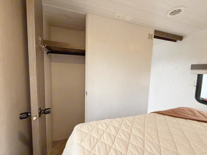 Cozy RV rental bedroom with a comfortable bed, open closet featuring a hanging rod and hooks, plus a sliding door and window.. Forest River Salem 2022