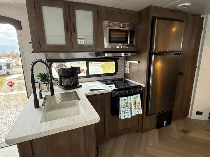 Modern RV rental kitchen featuring a full suite of appliances: microwave, stove, fridge, sink, and coffee maker. Ready for travel!. Forest River Salem 2022