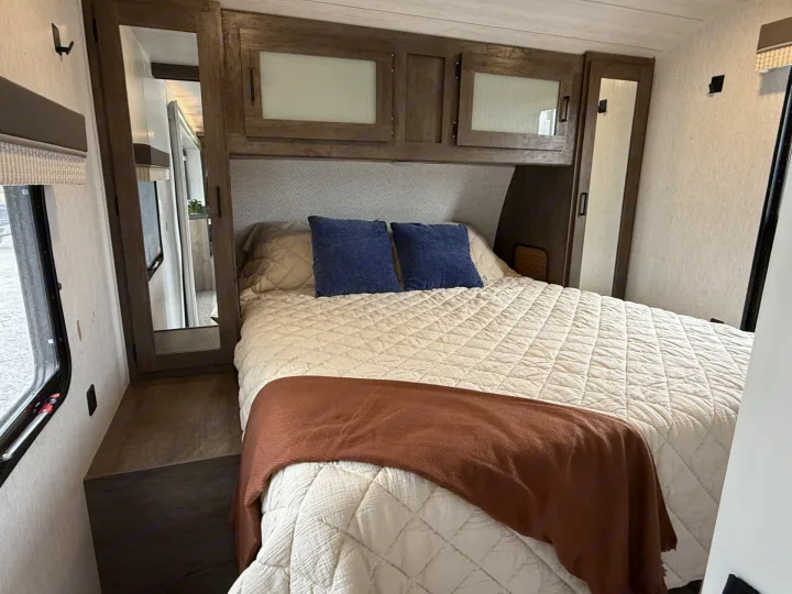 Cozy RV rental bedroom with a comfy bed, blue pillows, overhead storage, mirrored closets, and a side window.. Forest River Salem 2022