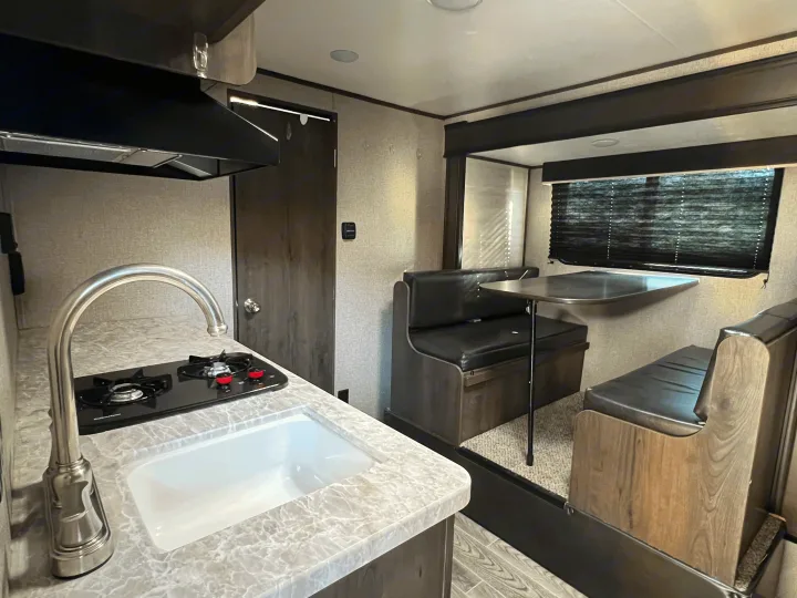 RV rental features a compact kitchen with a sink, two-burner stove, and comfortable dinette with window blinds.. jayco Jay Flight 2020