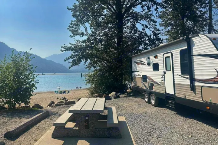 Serene rv rental campsite #36 by the lake with sandy beach, picnic table, and majestic mountain backdrop.. Starcraft Autumn Ridge 2018