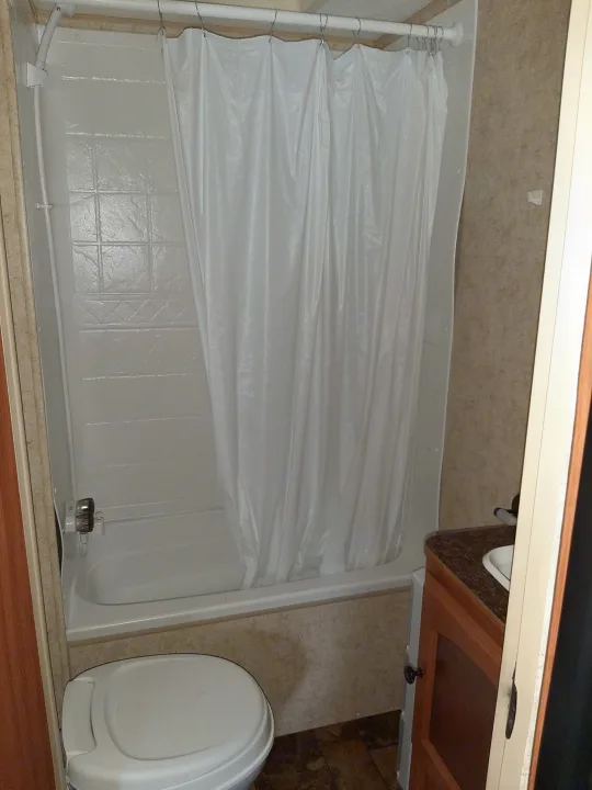 This RV rental bathroom features a white shower/tub combo with curtain, a toilet, and a small sink. Efficiently designed for travel.. Four Winds Breeze SS 2010