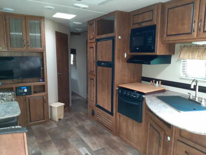Modern RV rental interior: kitchen with sink, stove, microwave, fridge; living area with TV & wood cabinets.. Crossroads RV Zinger 2017