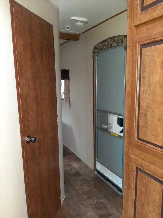 View of an RV rental interior hallway. Features a brown wooden door on the left, an open screened entry door on the right, and light wood-look flooring.. Crossroads RV Zinger 2017