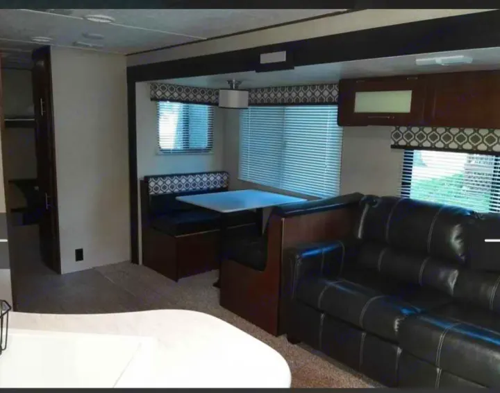Discover this comfy RV rental interior featuring a black leather couch, dinette, windows with blinds, and overhead storage cabinets.. Avenger ATI 2019
