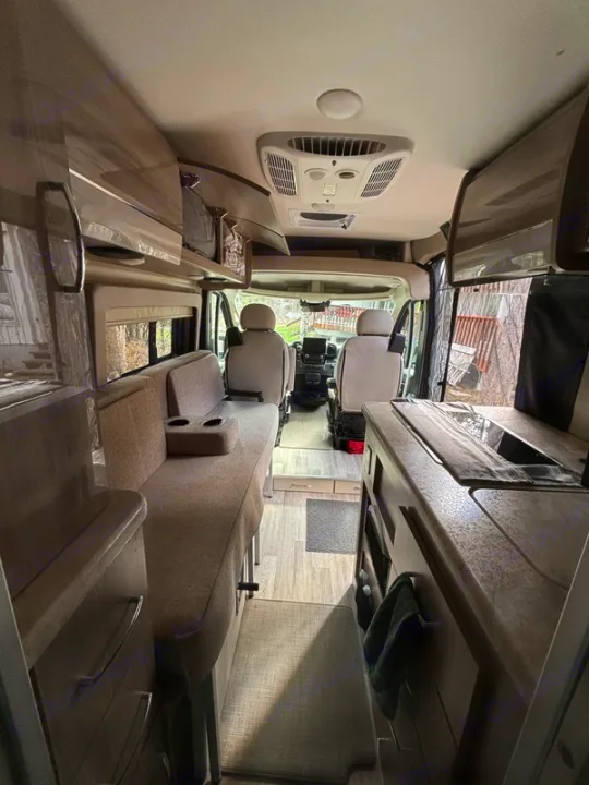 Looking forward inside a sleek rv rental camper van, revealing a compact kitchen, seating, and overhead storage.. Thor Scope 2024