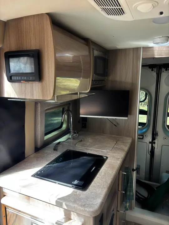 RV rental interior: a compact kitchen with Dometic stovetop, sink, microwave, and control panel, ideal for road trips.. Thor Scope 2024
