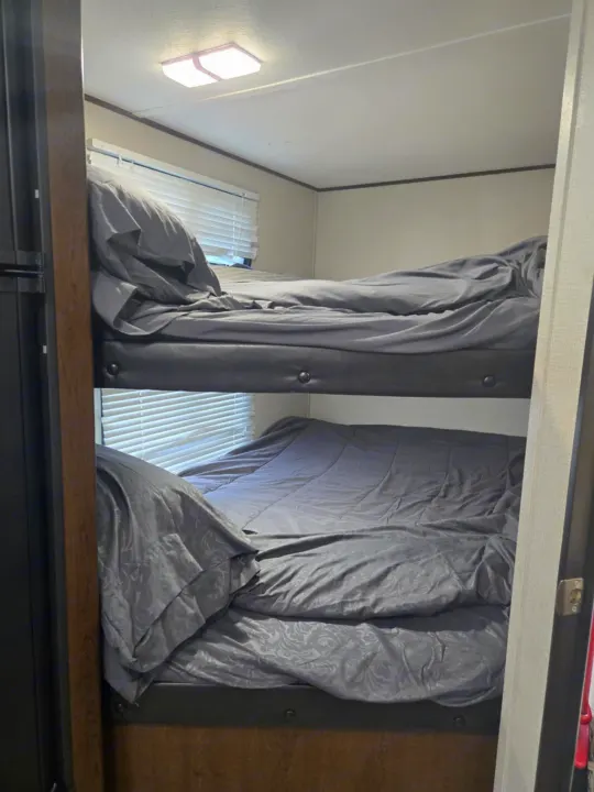 Cozy bunk beds with gray bedding and window blinds inside an RV rental, offering comfortable sleeping arrangements.. Avenger ATI 2019