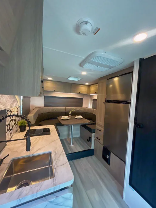 Explore this modern rv rental interior! Features a compact kitchen with marble countertops, sink, stovetop, dining booth, and fridge.. Forest River Sunseeker 2027