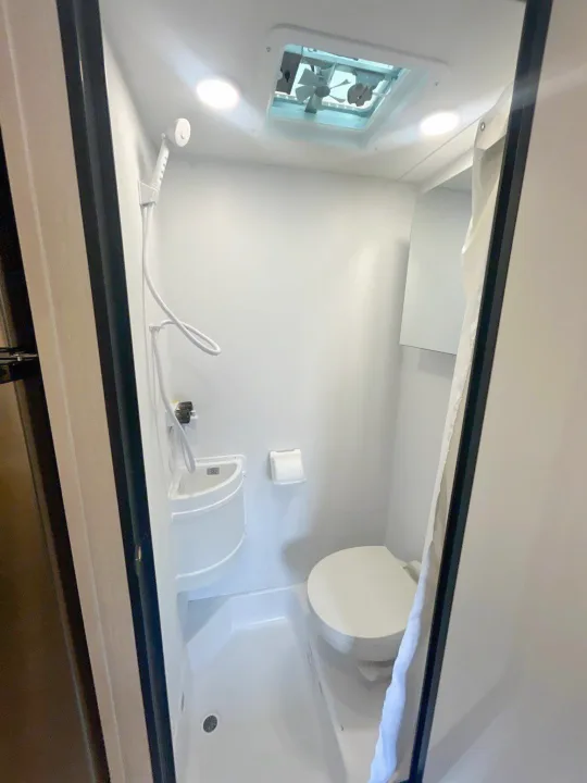 Compact RV rental bathroom features a shower, toilet, sink, and ceiling vent fan in a clean white space.. Forest River Sunseeker 2027