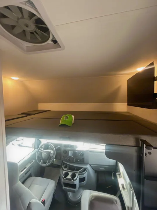 RV rental interior with an overhead bunk bed, cockpit, ceiling fan, and mounted TV. Ready for your next adventure!. Forest River Sunseeker 2027