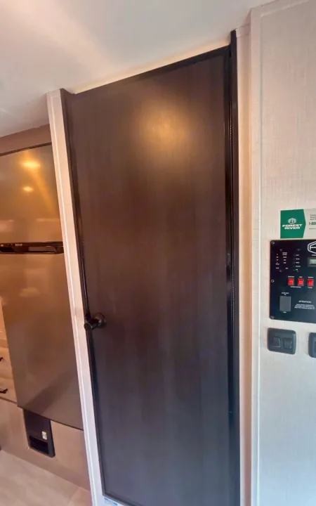 RV rental interior: A dark door, refrigerator, and control panel on the wall, showcasing typical RV amenities.. Forest River Sunseeker 2027