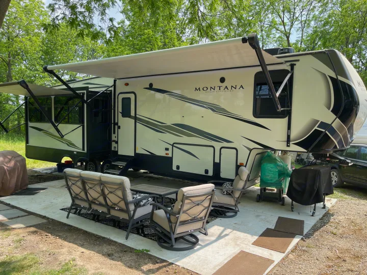 Luxury fifth-wheel RV rental at a scenic campsite with an inviting outdoor patio setup.. Keystone RV Montana High Country 2021