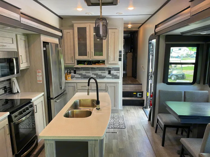 Inside a modern RV rental: sleek kitchen with island sink, stainless appliances, and cozy dining space.. Keystone RV Montana High Country 2021