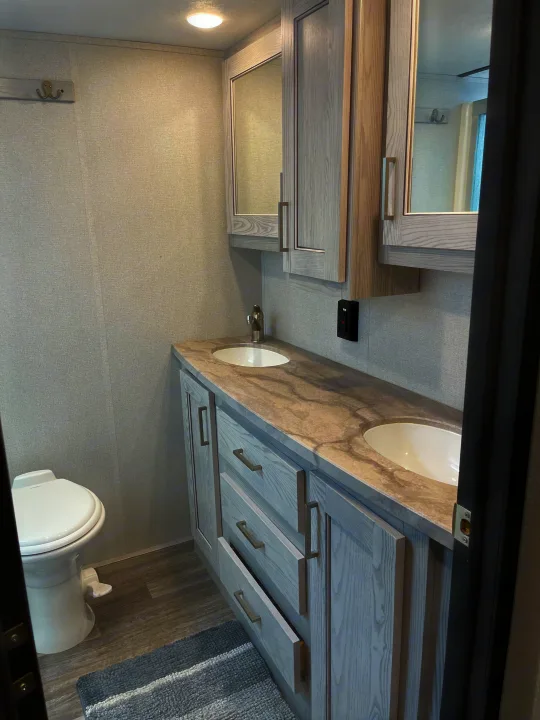 Clean and modern RV rental bathroom featuring a double vanity, two sinks, toilet, and light-toned decor.. Keystone RV Montana High Country 2021