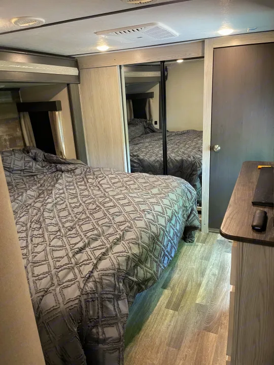 Modern rv rental bedroom with gray patterned bedding, mirrored closet, wood floor, and overhead lights for comfortable travel.. Keystone RV Montana High Country 2021