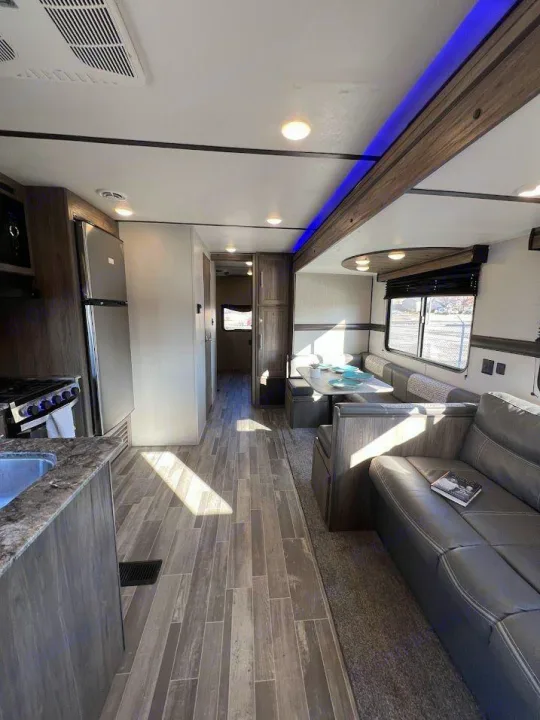 View of an RV rental's spacious interior with wood-look floors, a kitchen, dinette, sofa, and modern lighting.. Crossroads RV Zinger 2021