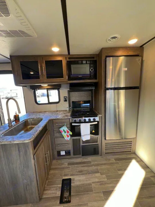 RV rental kitchen interior: corner sink, stove, microwave, and fridge in a modern gray finish.. Crossroads RV Zinger 2021