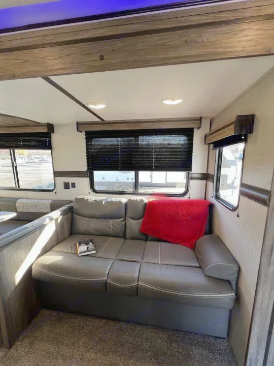 Comfortable RV rental living space with a modern gray sofa, red accent pillow, and bright windows. Ready for your adventures!. Crossroads RV Zinger 2021