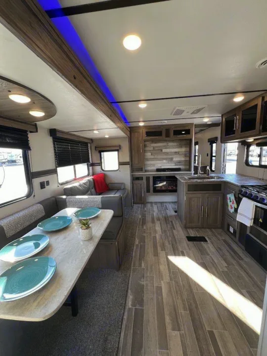 Modern RV rental interior: spacious living area with kitchen, dining, sofa, and fireplace. Bright, comfortable design for road trips.. Crossroads RV Zinger 2021