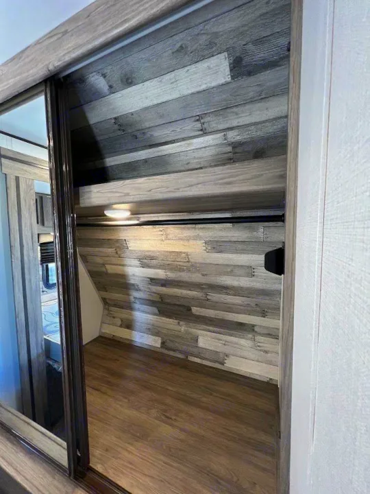 RV rental closet with sliding doors, wood-look walls, a hanging rod, shelf, and light, offering compact storage.. Crossroads RV Zinger 2021