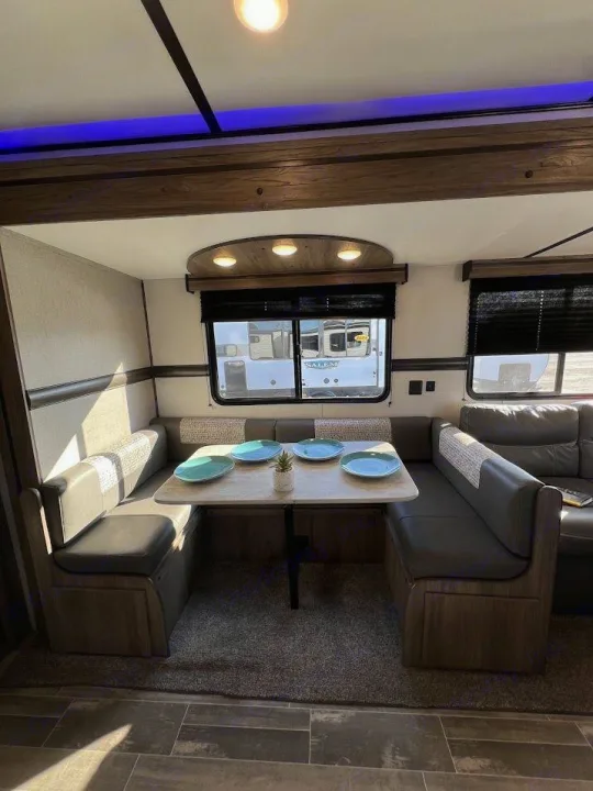 Cozy rv rental dinette with comfortable bench seating, set table, windows & blue accent lighting, ready for meals.. Crossroads RV Zinger 2021