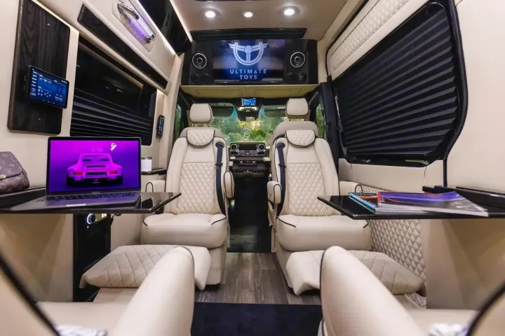 Inside a luxurious RV rental with quilted leather seats, large screen, and laptop workspace for premium travel comfort.. Ultimate Toys Ultimate Coach 2024