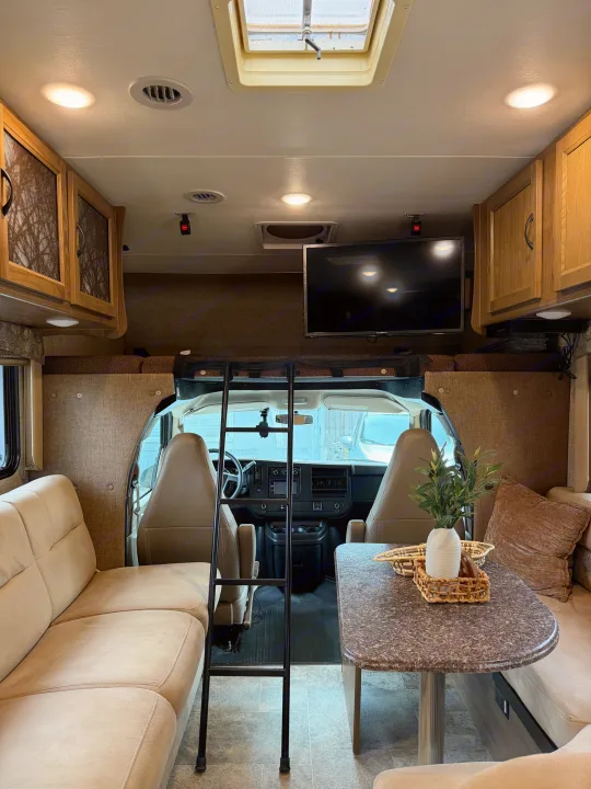 Bright and inviting rv rental interior with a comfortable living area, dining table, overhead bunk access, and front cabin view.. Coachmen Freelander 26 RS 2017