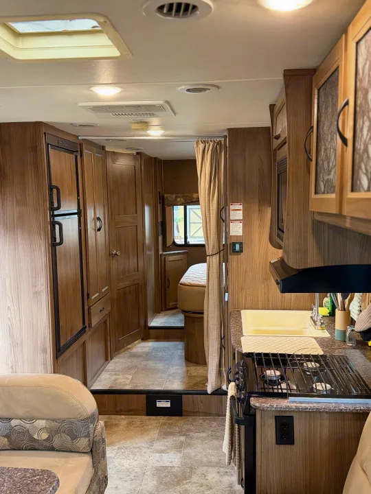 Explore this clean, well-equipped RV rental interior! Features include a kitchen, living area, and cozy bedroom with wood cabinetry.. Coachmen Freelander 26 RS 2017