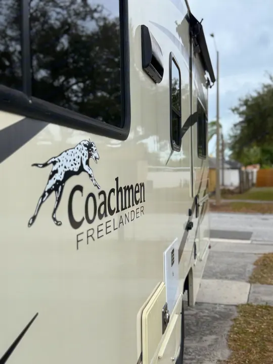 Angled view of a cream-colored Coachmen Freelander RV, showcasing its logo and features. Ideal for your next rv rental adventure.. Coachmen Freelander 26 RS 2017