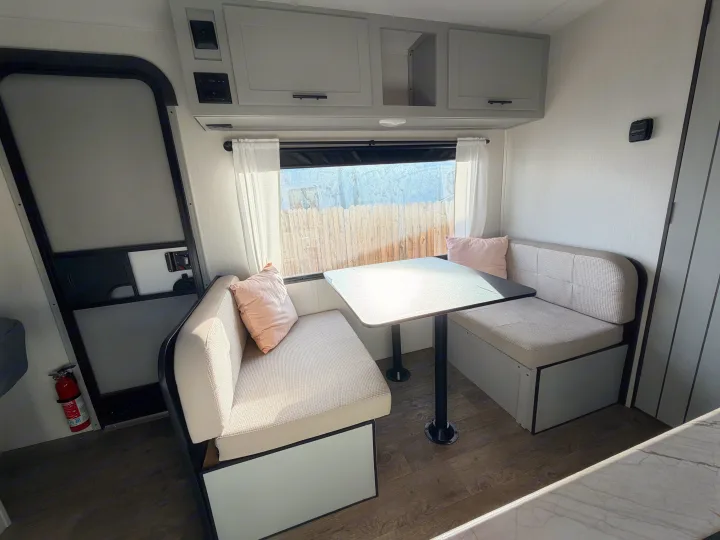 Bright RV rental dinette features light upholstered benches, a table, and modern overhead cabinets. Ideal for small space dining.. Forest River Vibe 2021