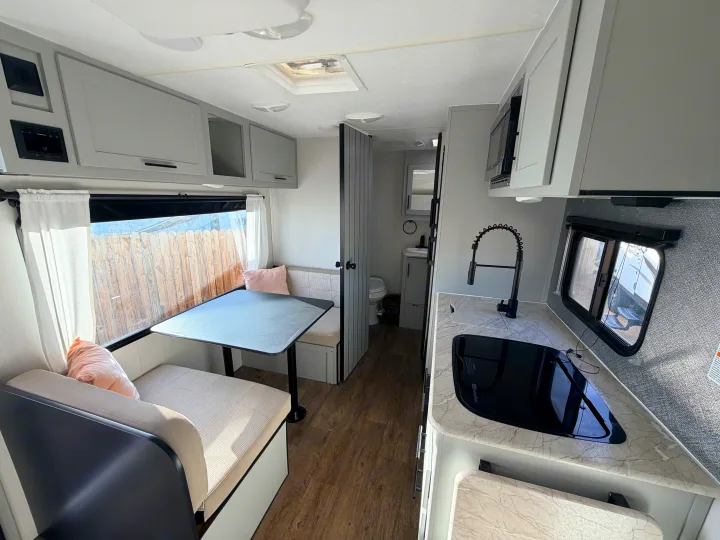 RV rental with a bright, modern interior. Features include a dinette, compact kitchen with black appliances, and light grey cabinets.. Forest River Vibe 2021