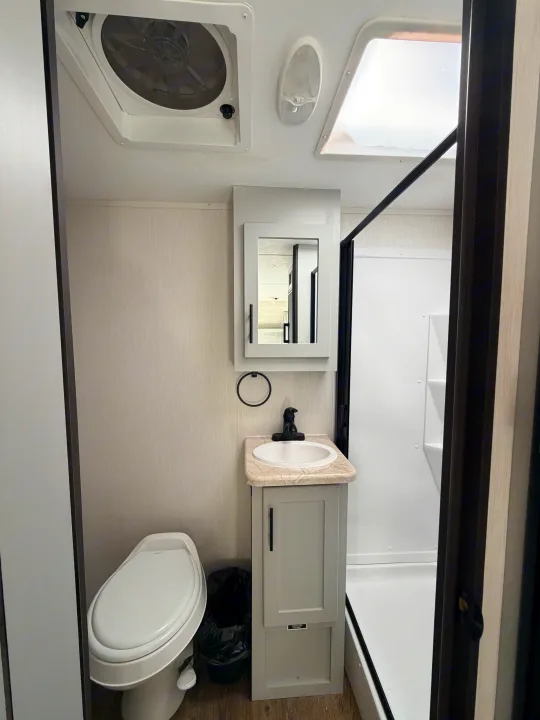 Clean, compact rv rental bathroom: features a toilet, vanity with sink, mirror, shower stall, ceiling fan, and skylight.. Forest River Vibe 2021